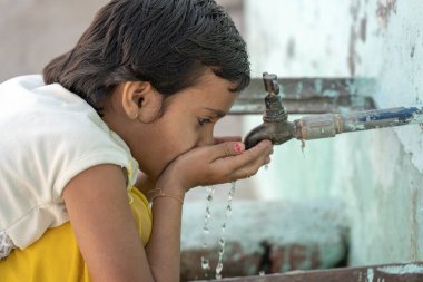 RISHIKESH, INDIA - 06, 2018: Hintli susamış bir kızın portresi Rishikesh, Hindistan 'da sokak musluğundan su içiyor