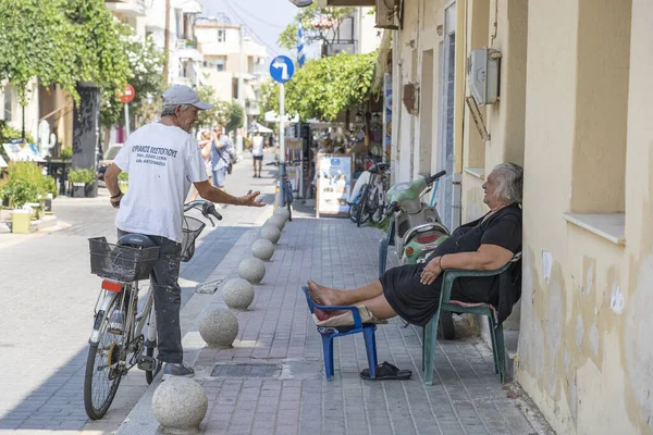 Kos Adası, Yunanistan - Eylül 04, 2019: Yunanistan 'ın Kos adasındaki eski kentin önünde oturan yaşlı kadın ve bisikletli adam
