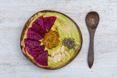 Hindistancevizi kabında yeşil avokado smoothie içinde ejderha meyvesi, tutku meyvesi, badem gevreği, hindistan cevizi cipsi ve chia çekirdeği kahvaltıda yakın çekim. Sağlıklı yeme, süper yemek kavramı. Bali, Endonezya