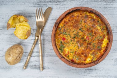Sebzeli frittata ile seramik kase, basit vejetaryen yemeği. Tahta masada domates, biber, soğan ve peynirli frittata, yakın çekim. İtalyan omleti, üst manzara.