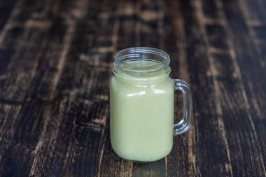Avokado 'dan taze yeşil smoothie, ahşap arka planda cam bardakta muz ve bal, yakın plan. Sağlıklı beslenme kavramı