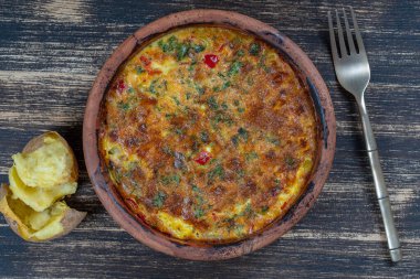 Sebzeli frittata ile seramik kase, basit vejetaryen yemeği. Tahta masada domates, biber, soğan ve peynirli frittata, yakın çekim. İtalyan omleti, üst manzara.