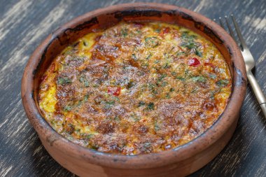 Sebzeli frittata ile seramik kase, basit vejetaryen yemeği. Tahta masada domates, biber, soğan ve peynirli frittata, yakın çekim. İtalyan omleti, üst manzara.