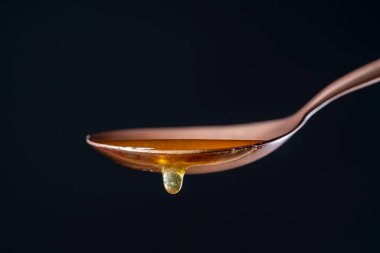 Ballı kaşık. Kalın bal damlıyor ve bir metal kaşıktan aşağı akıyor, bir damla, siyah arkaplanda, kapat