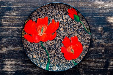 Dekoratif seramik tabak, kırmızı haşhaş, ahşap arka planda boyalı tabak, yakın plan, üst manzara. Akrilik boyalarla boyanmış dekoratif porselen tabaka, el işi, nokta boyası.