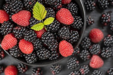 Taze organik böğürtlen ve ahududu arkaplanı, yakın plan. Bir sürü olgun, sulu, siyah tabakta çiğ meyve. Üst manzara böğürtlen ve ahududu
