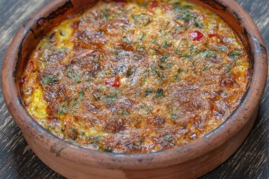 Sebzeli frittata ile seramik kase, basit vejetaryen yemeği. Tahta masada domates, biber, soğan ve peynirli frittata, yakın çekim. İtalyan omleti, üst manzara.