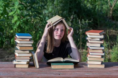 Genç bir kız kitap okuyor ve bahçedeki tahta bir masada kitap yığınıyla hayaller kuruyor. Ev eğitimi kavramı