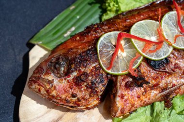 Taze yeşil salatalı kızarmış balık ve Endonezya, Bali limonu, yakın çekim. Restoranda ahşap tabakta limonlu kızarmış deniz balığı.