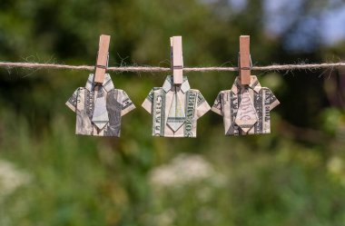 Asılı yeşil doğa üzerine dolar banknotundan yapılmış Origami gömleği. İpe asılmış dolar banknotları. Kapatın. Dolar Tişörtü