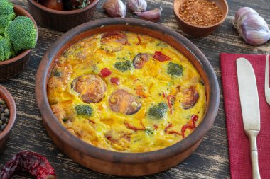 Sebzeli frittata ile seramik kase, basit vejetaryen yemeği. Yumurta, domates, biber, soğan, brokoli ve peynirli frittata, ahşap masaya, yakın çekim. İtalyan omleti.
