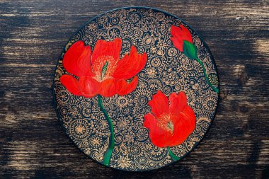 Dekoratif seramik tabak, kırmızı haşhaş, ahşap arka planda boyalı tabak, yakın plan, üst manzara. Akrilik boyalarla boyanmış dekoratif porselen tabaka, el işi, nokta boyası.