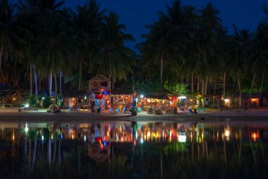 KOH PHANGAN, THAILAND - Mayıs 03, 2019: Sahil barı, hindistan cevizi palmiyesi ağaçları, deniz suyu ve gece kulübü, Tayland 'ın Koh Phangan adasındaki deniz suyuna yansımaktadır.