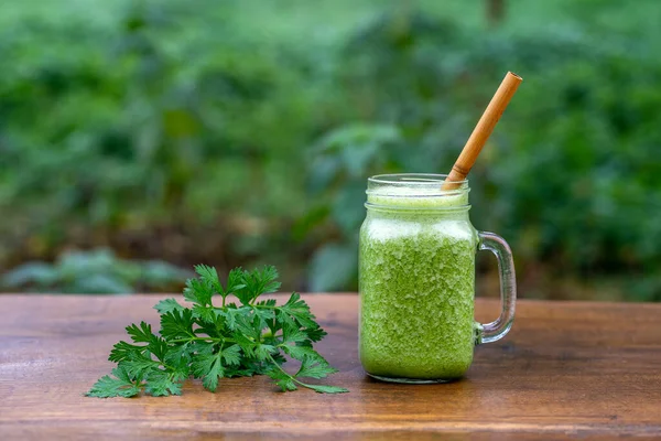 Green smoothie of parsley, avocado, honey and banana in a glass mug on a wooden table in a garden cafe, close-up. Healthy food concept