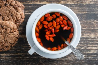 Beyaz sabah goji kahvesi, ahşap masanın üstünde, üst manzara, yakın çekim. Kırmızı böğürtlenli sade sıcak kahve.