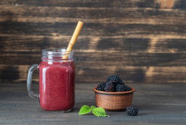Ahşap arka plandaki cam kavanozda taze böğürtlen smoothie, yakın çekim. Sağlıklı gıda konsepti