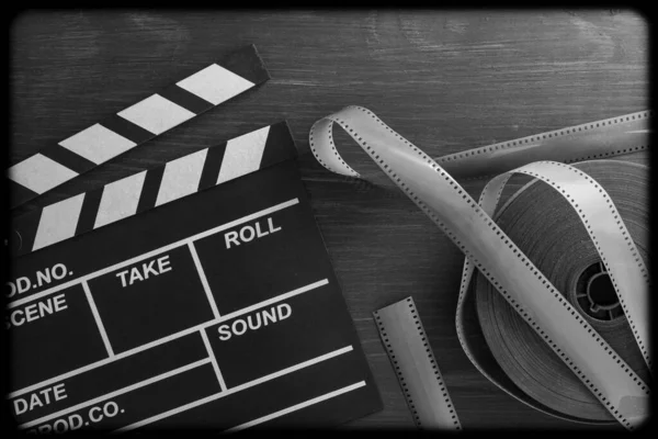 Vintage photo of movie clapper and film strip on wooden background, close up, top view, black and white