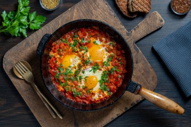 Shakshuka kahvaltıda kızartma tavasında, kapat. Haşlanmış yumurta, soğan, dolma biber, zeytinyağı, dökme demir tavada kırmızı domates ve maydanoz karışımı. Akdeniz mutfağı