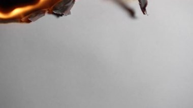 Siyah arka planda beyaz kağıt yanıyor, yakın çekim. Kağıt yanar, duman çıkarır ve küle dönüşür. Ateş ve kağıt