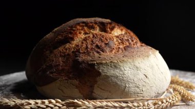 Tahta kesme tahtasının üzerinde buğday kulaklı taze ekşi ekmeğin yuvarlak somunu kapanıyor, dönüyor. Rustik ekşi ekmek. Evde sağlıklı ekşi ekmek pişirmek.