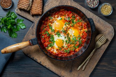 Shakshuka kahvaltıda kızartma tavasında, kapat. Haşlanmış yumurta, soğan, dolma biber, zeytinyağı, dökme demir tavada kırmızı domates ve maydanoz karışımı. Akdeniz mutfağı