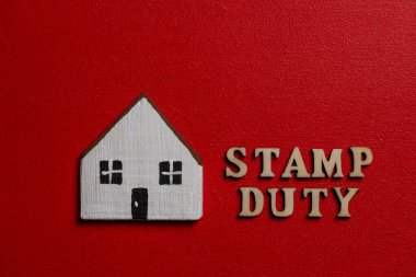 Kırmızı arka planda beyaz ahşap evin yanındaki ahşap harflerden yapılmış yazıt pulu vergisi, kapat. Damga Vergisi, gayrimenkul ve arazi alımının yanı sıra diğer işlemlerin vergisidir.