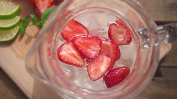 Halves of strawberries in a decanter with ice and water top view — Stock Video