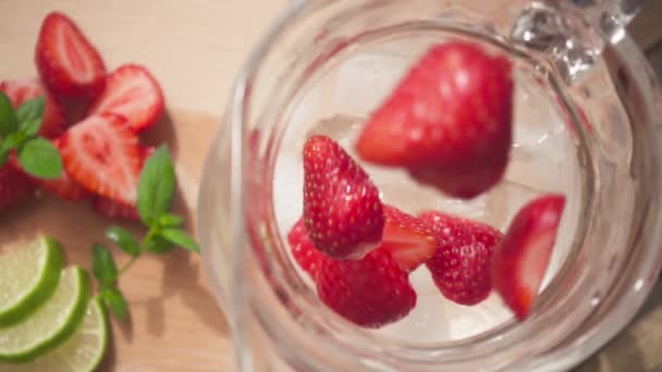 Sliced strawberries fall into a carafe with ice and water slow motion — Stock Video