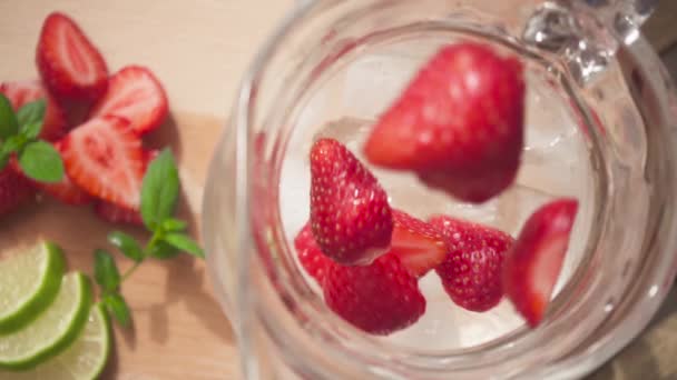 Fraises tranchées tombent dans une carafe avec de la glace et de l'eau au ralenti — Video