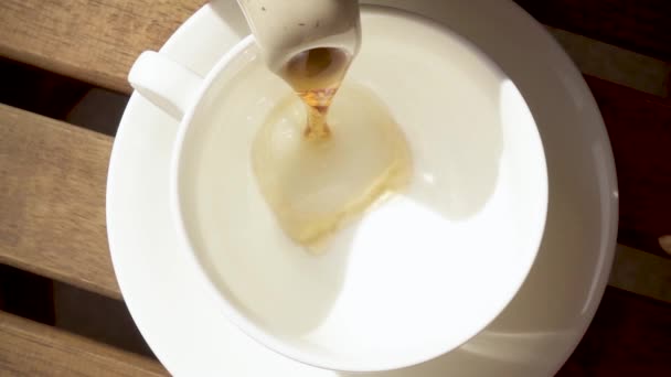 Біла порцелянова чашка на блюдці на дерев'яному столі з гарячим напоєм повільний рух — стокове відео
