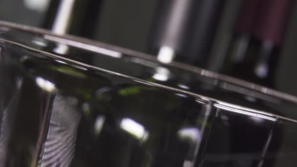 Wijn giet in een glas tegen de achtergrond van flessen — Stockvideo