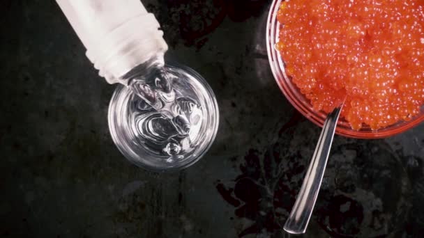 Cámara lenta vierta el vodka en un vaso sobre la mesa con vista superior de caviar — Vídeos de Stock