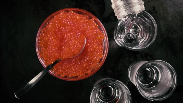 Slow motion giet de wodka in een glas op tafel met kaviaar bovenaanzicht — Stockvideo