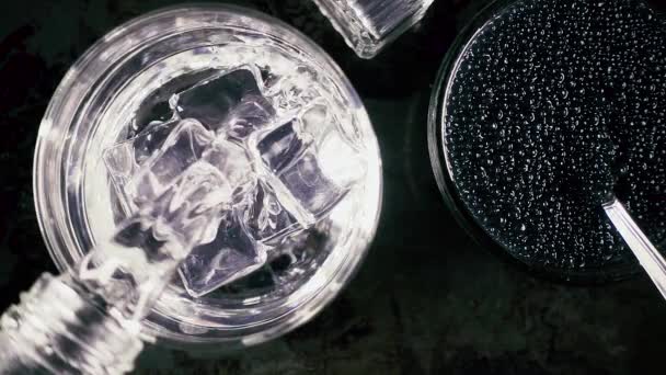 Vodka en cámara lenta en un vaso y caviar sobre un fondo negro — Vídeo de stock