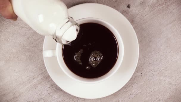 Slow motion giet de melk in bovenaanzicht van zwarte koffie — Stockvideo