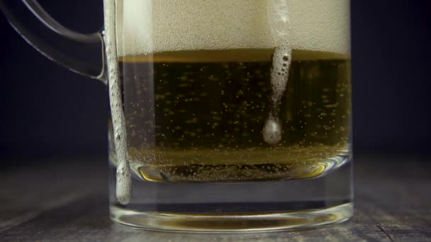 Cerveza ligera de cámara lenta en una taza de vidrio sobre un fondo gris — Vídeo de stock