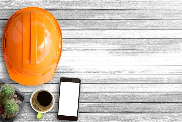 Orange safety helmet,cactus and cup of coffee on white wood tabl