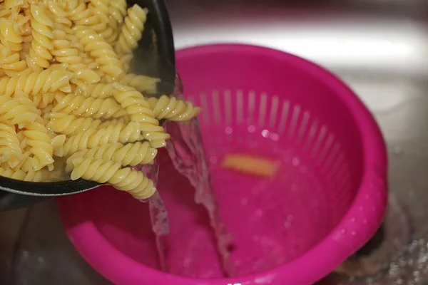 fresh cooking noodles are falling in a pink plastic sieve