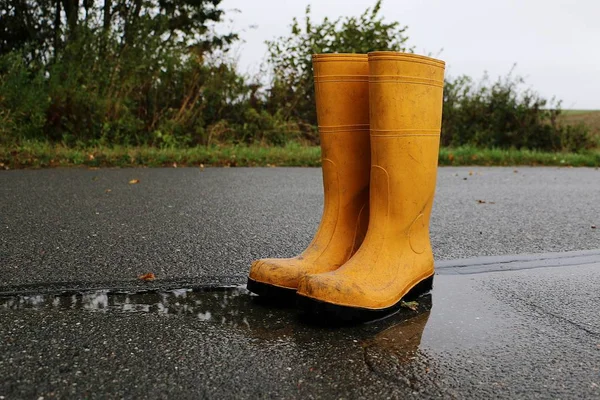 A pair of yellow rubber boots stand in a puddle on the street on a rainy day