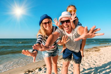 Kumsalda mutlu bir aile. İnsanlar yaz tatilinde eğleniyor. Baba, anne ve çocuk mavi deniz ve gökyüzü arka planına karşı. Tatil seyahati kavramı