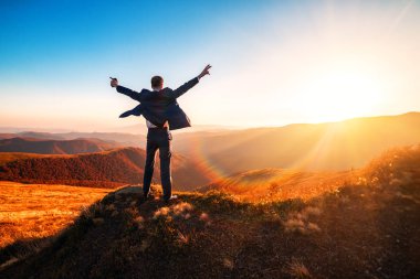Takım elbiseli başarılı adam güzel bir günbatımında ellerini kaldırdı.