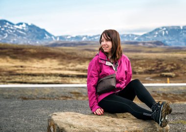 Mor ceketli kız taşın üzerinde oturuyor.