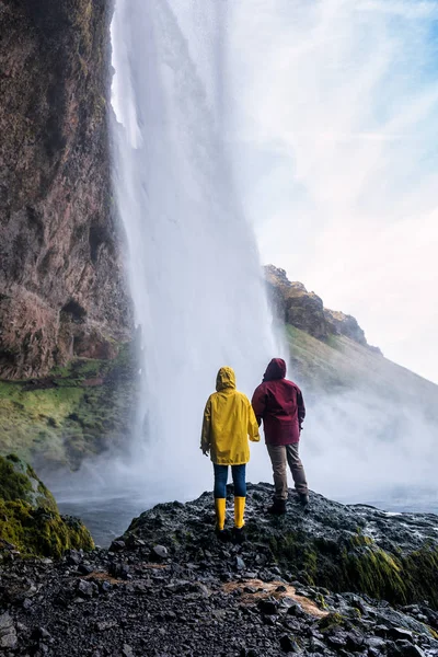 Casal em roupas brilhantes olha para uma cachoeira islandesa — Fotografia de Stock