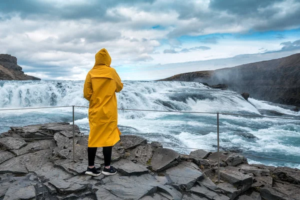 Het meisje in een gele regenjas kijkt naar de waterval — Stockfoto