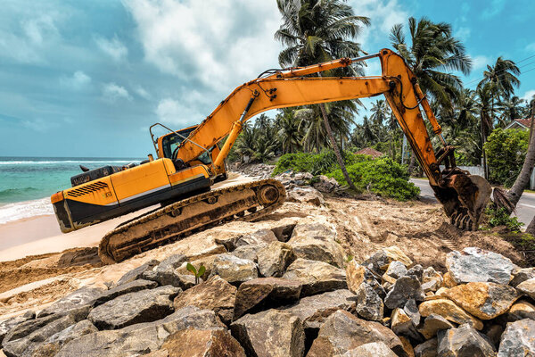 yellow excavator strengthens the ocean shore on Sri Lanka