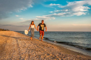 Gün batımında kumsalda el ele tutuşan mutlu çift.