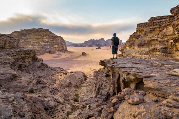 Sırt çantalı adam Ürdün 'deki Wadi Rum çölünde kayanın üzerinde duruyor.