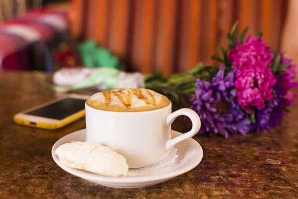 Fincan sıcak kakao veya Cappuccino ya da sütlü kahve hatmi ve çiçek ve telefon bir tablo ile