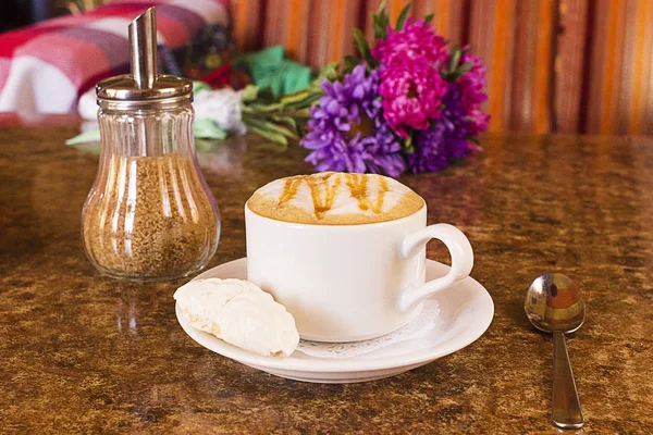 Fincan sıcak kakao veya Cappuccino ya da sütlü kahve hatmi ve bir masaya çiçek