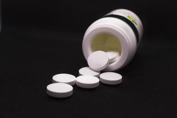 Pílulas brancas espalhadas de uma garrafa em um fundo preto . — Fotografia de Stock